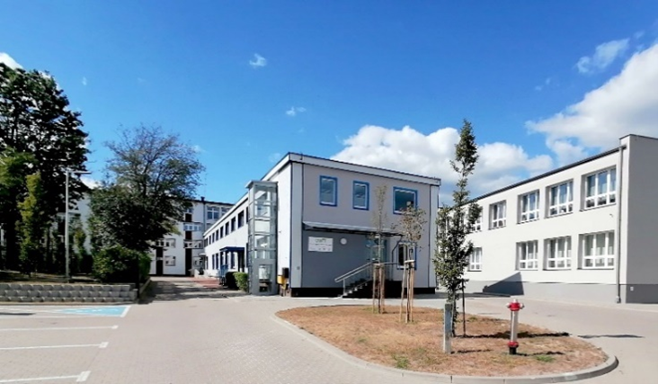 Kompleks jednopiętrowych budynków z białą elewacją i miejscami parkingowymi.