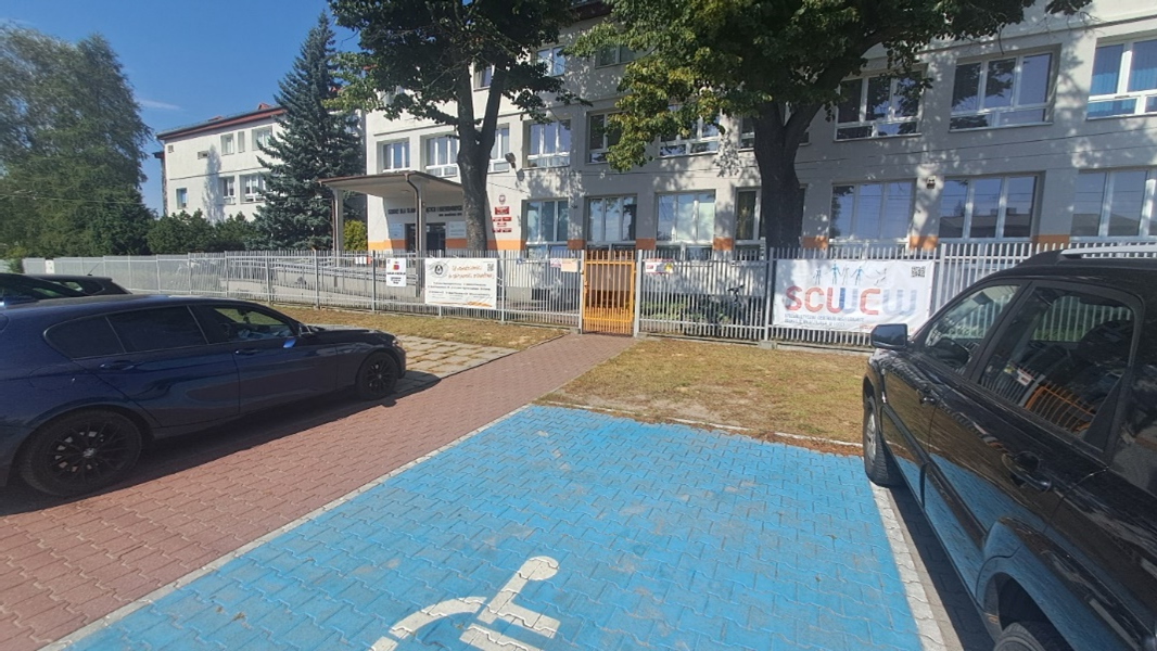 Kompleks dwupietrowych budynków z białą elewacją i miejscami parkingowymi.