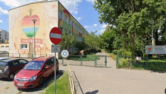 Dwupietrowy budynków z beżową elewacją i miejscami parkingowymi.