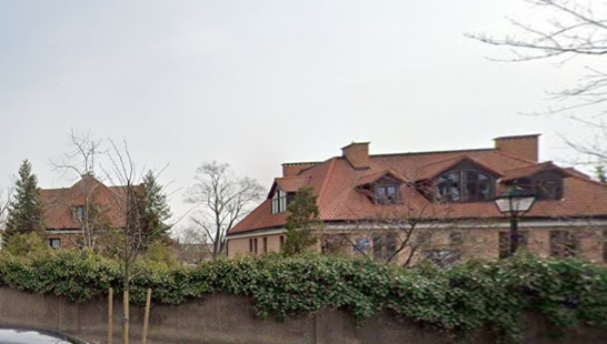 Kryty czerwoną dachówką duży budynek otoczony żywopłotem