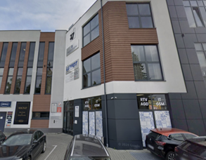 Nowoczesny budynek usługowo-biurowy z jasną elewacją i dużymi oknami, z lokalami na parterze oraz zaparkowanymi samochodami przed wejściem na parkingu.