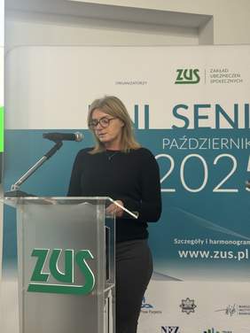 Pokaż zdjęcie: Osoba stojąca przy mównicy z napisem ZUS. W tle baner informujący o dniach seniora.